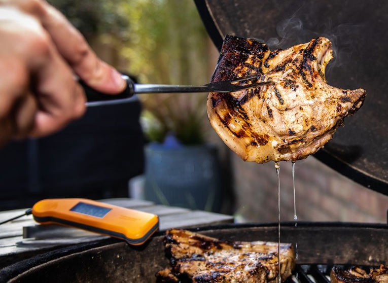 Juicy Pork on a bbq with an orange Thermapen ONE one the side
