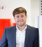 Jason Webb in a blue checkered suit standing in an office setting with red and white decor.
