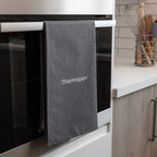 Gray towel with 'Thermapen' logo hanging on an oven handle in a kitchen.