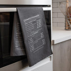 Grey tea towel with temperature chart hanging on a kitchen oven door.