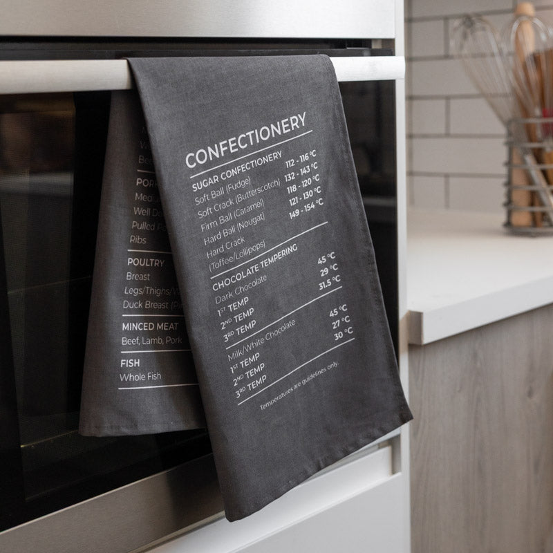 Grey tea towel with temperature chart hanging on a kitchen oven door.