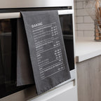 Gray tea towel with baking temperature chart hanging on an oven door.
