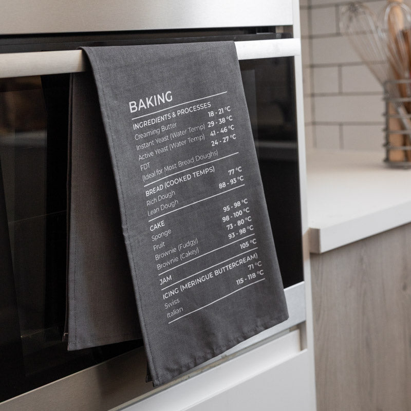 Gray tea towel with baking temperature chart hanging on an oven door.