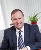 Peter Webb in a suit and tie sitting in an office setting with a plant in the background