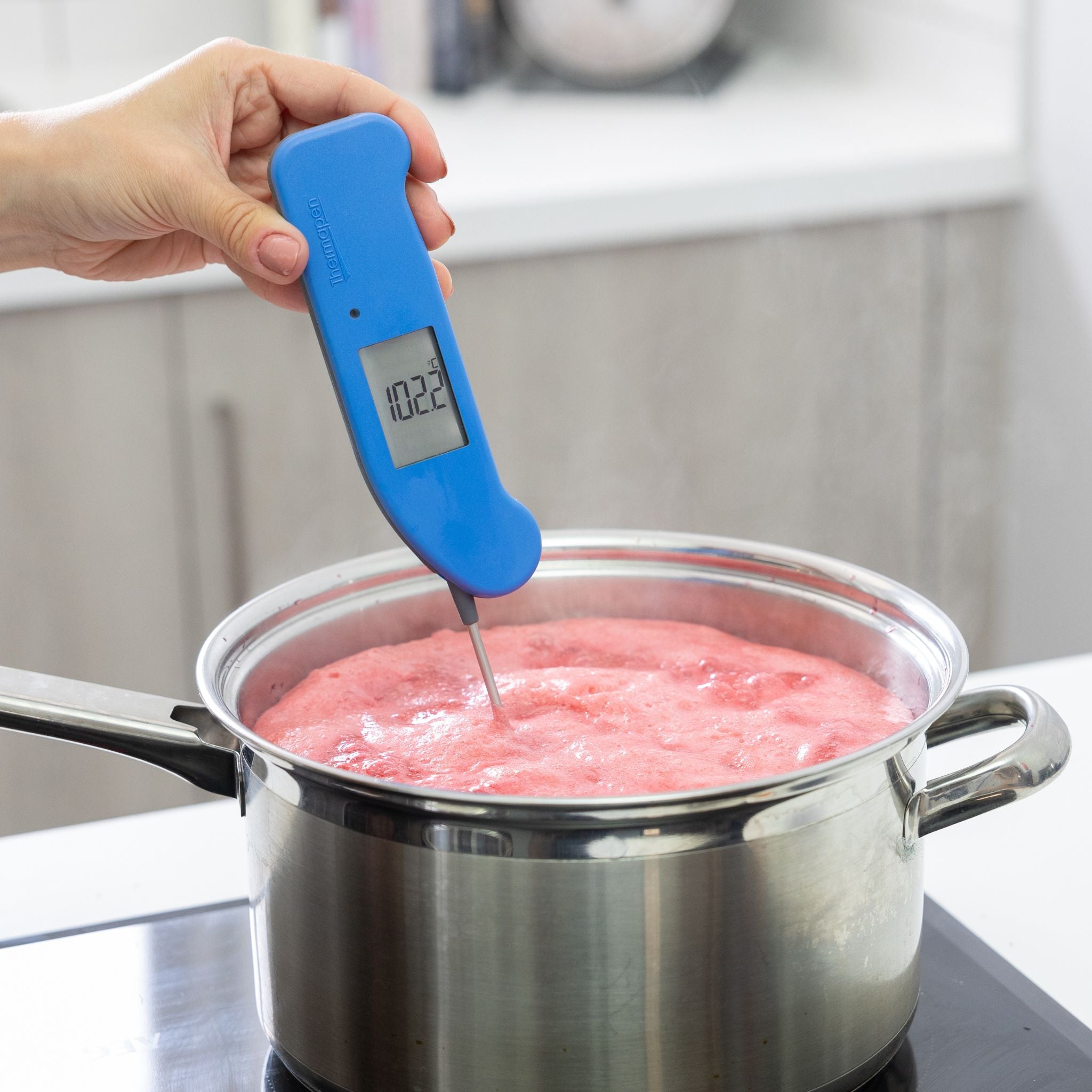 Blue Thermapen ONE being used to check the temperature of a pot of jam on a stove.