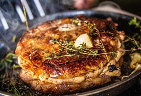 Sizzling Cote de Boeuf steak with garlic and fresh thyme in a hot cast iron pan.