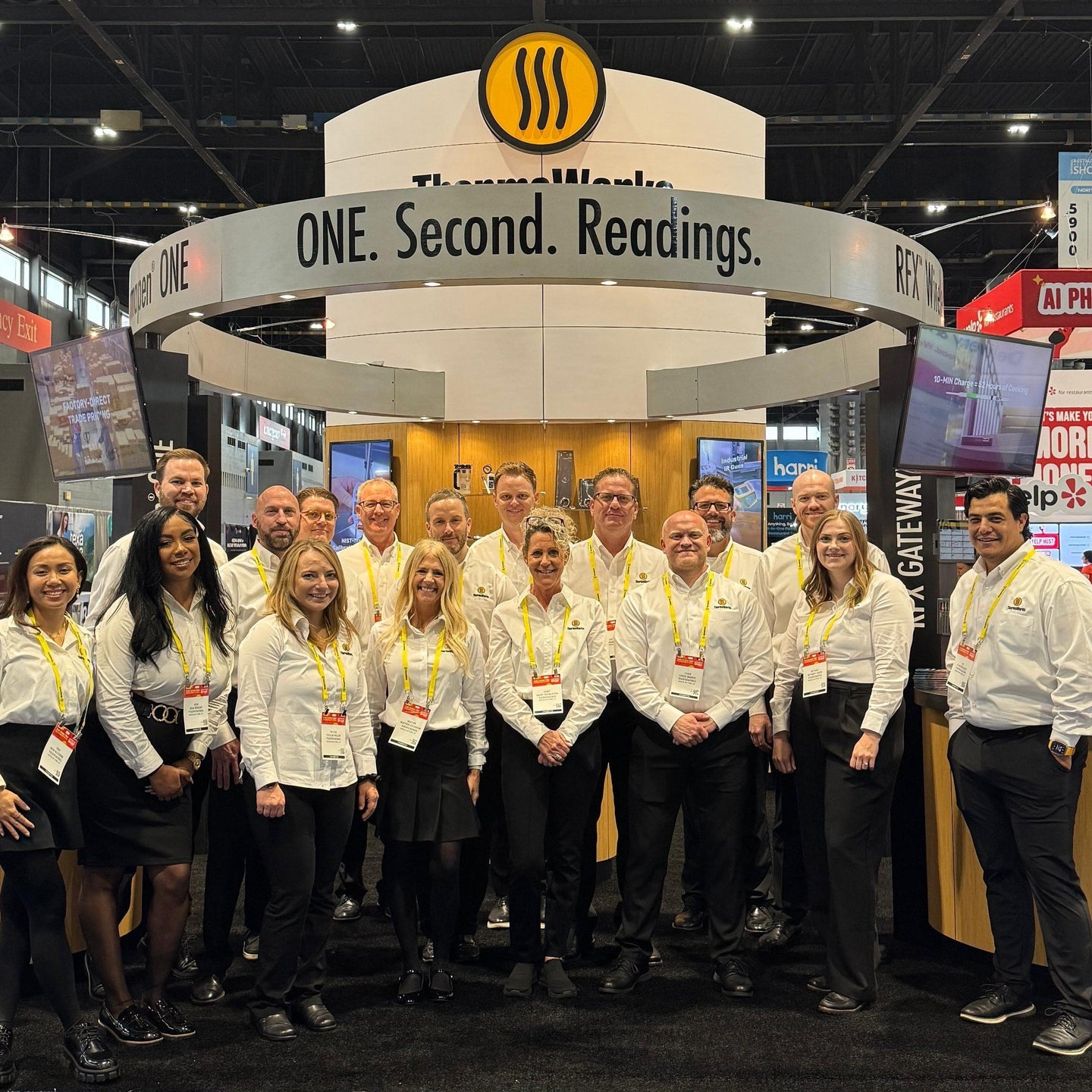Group of people in white shirts standing in front of a booth with a logo at an event.