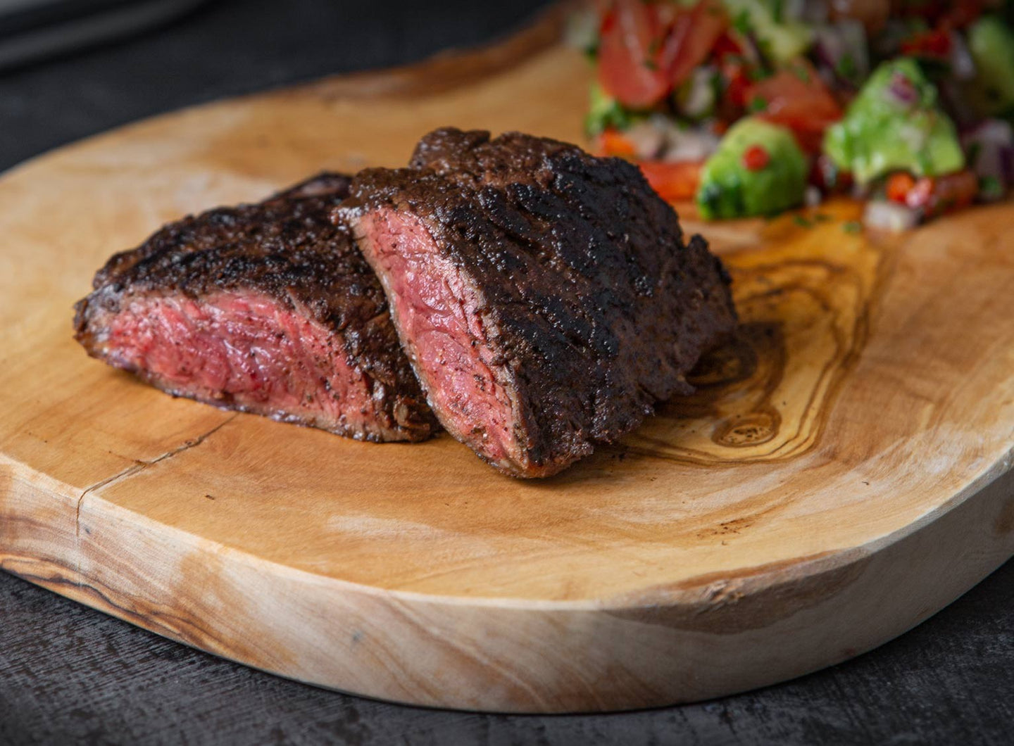 Sliced hanger steak on a wooden board with avocado salsa