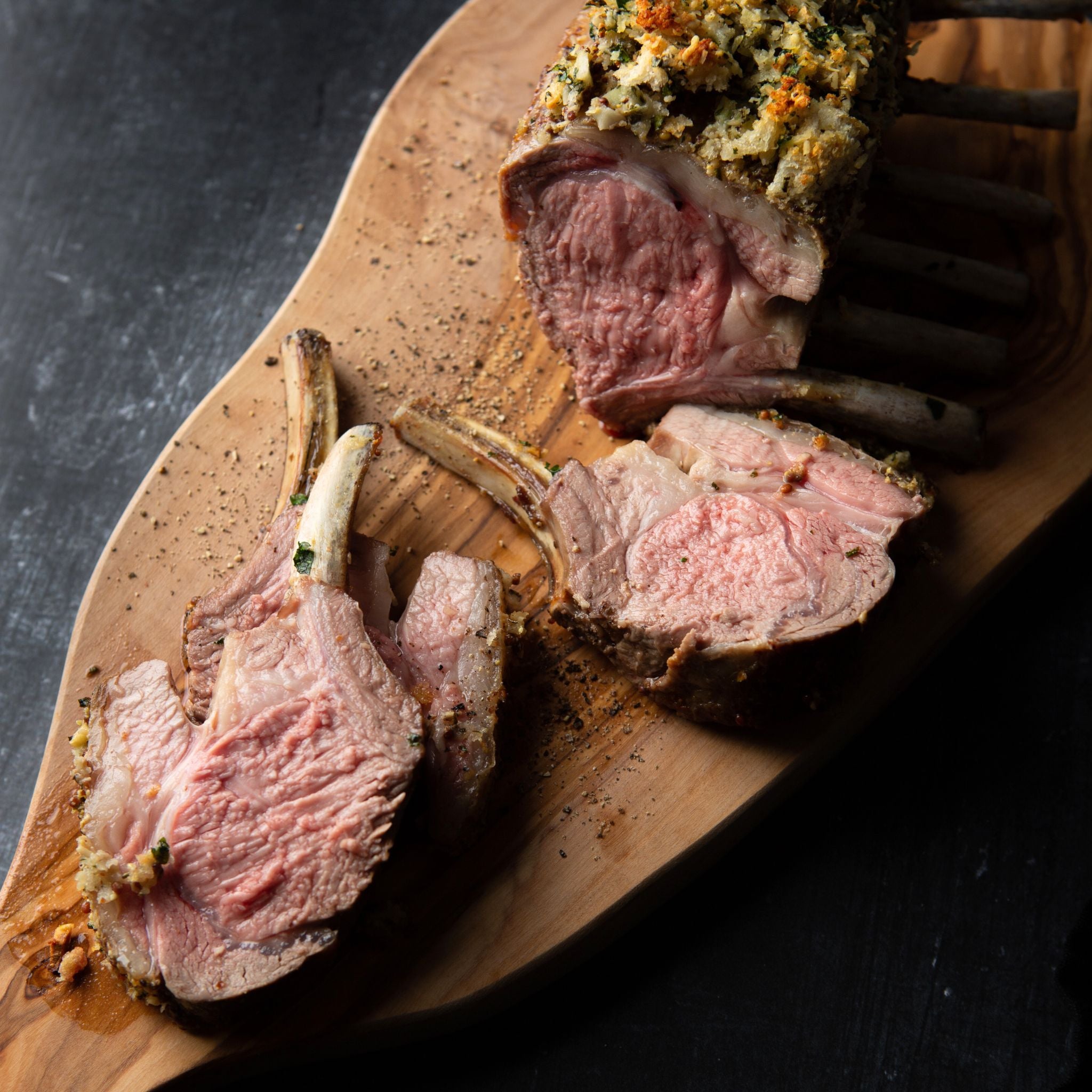 Sliced roasted lamb on a wooden cutting board with a dark background