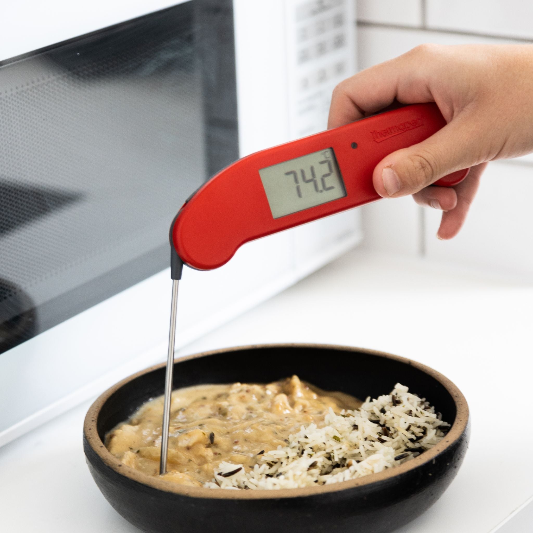 Red digital thermometer reading 74.2 degrees being used to check the temperature of food in a bowl