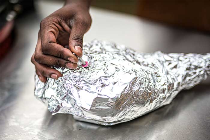 A person inserting an RFX meat probe into a lamb leg wrapped in foil
