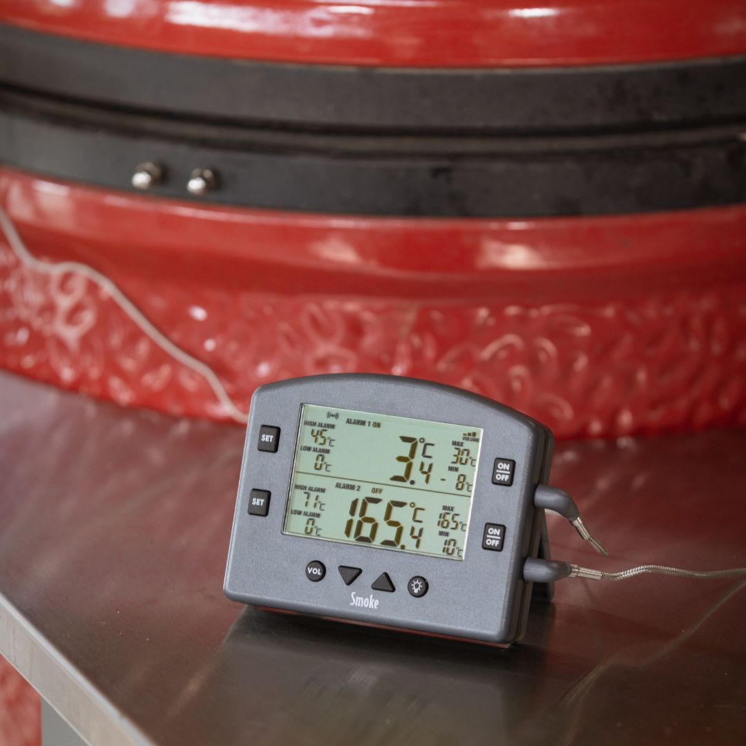 smoke thermometer on a reflective BBQ table with a red ceramic barbecue in the background