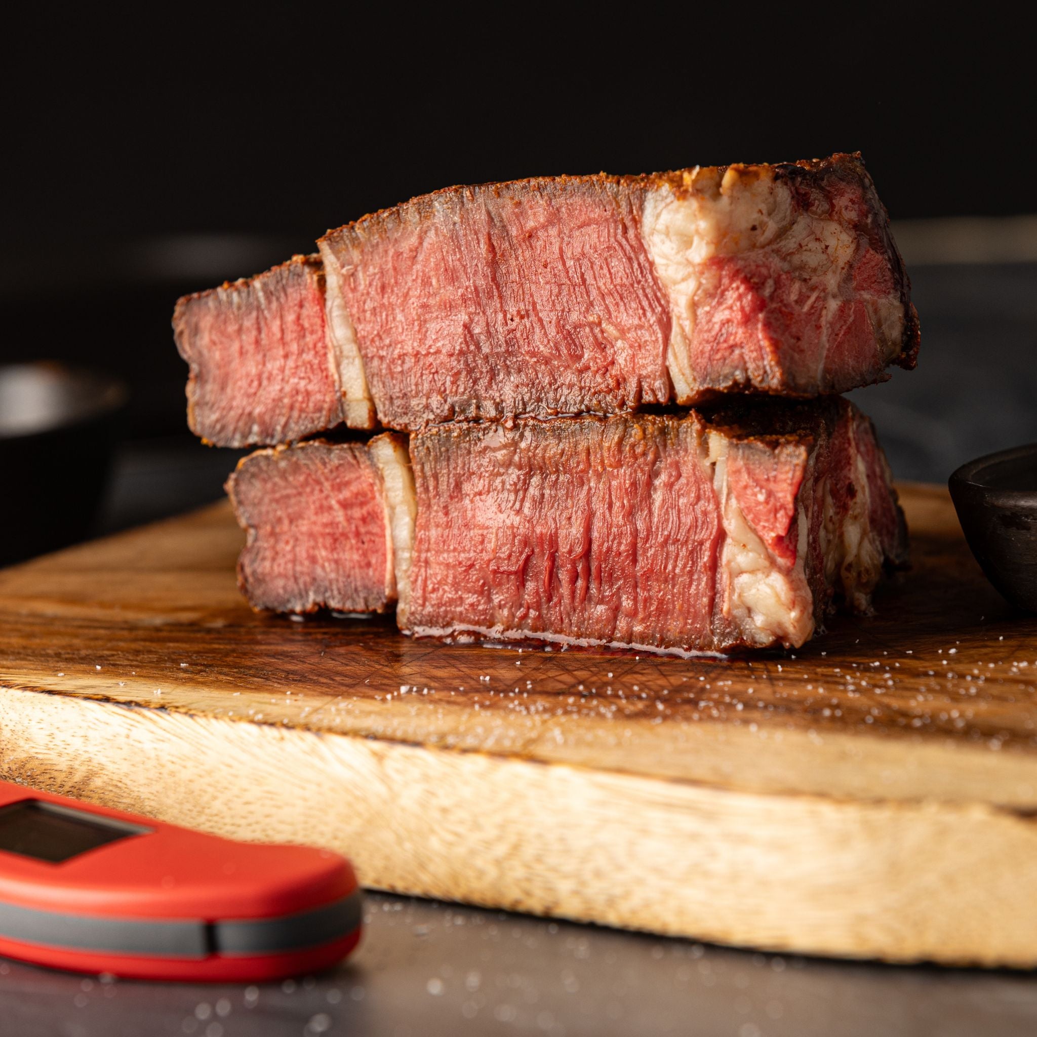 Sliced piece of beef, cooked medium rare, on a wooden cutting board with a red thermapen one thermometer in the foreground.