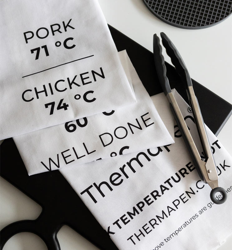 Tea towels printed with temperatures and cooking tongs on a white countertop