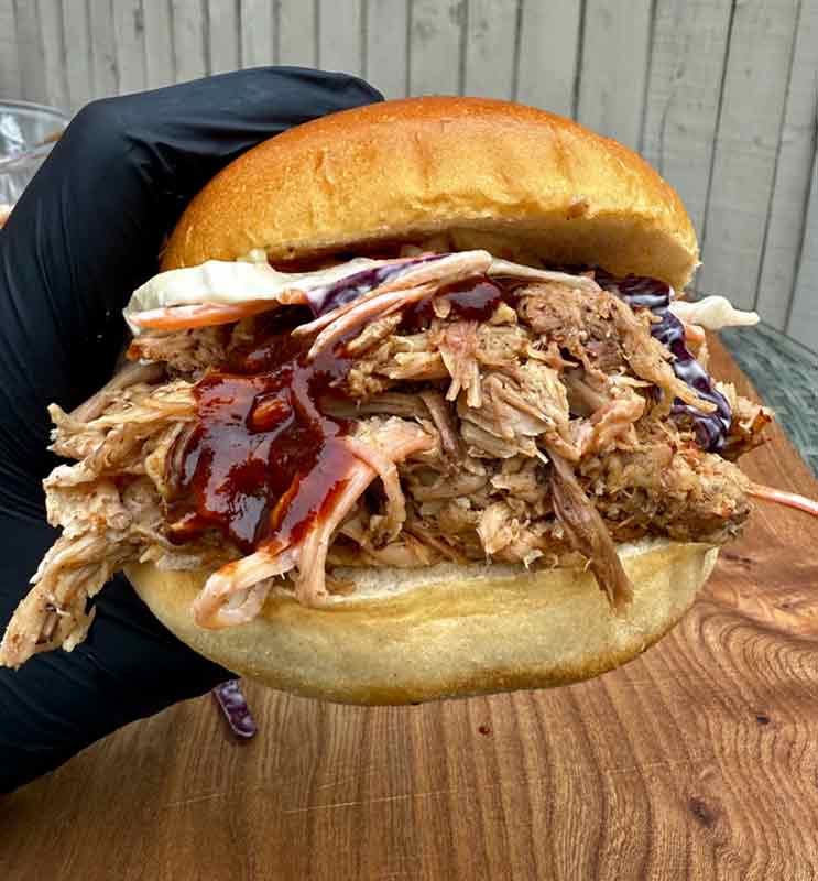 Tender BBQ pulled pork, loaded into buns with coleslaw and BBQ sauce in hand