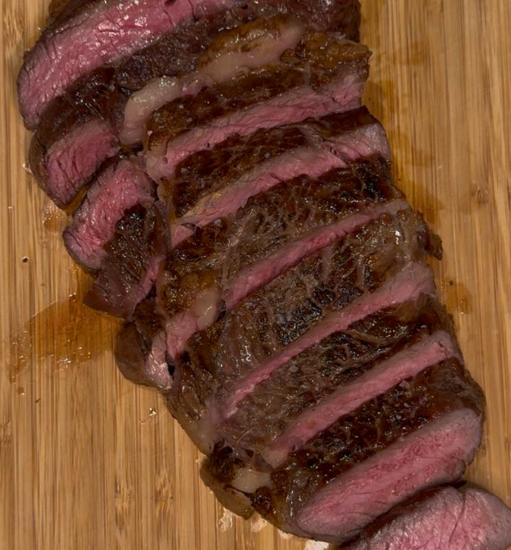 Perfectly cooked and sliced ribeye steak on a wooden cutting board, revealing a medium-rare pink center, achieved with accurate temperature monitoring.