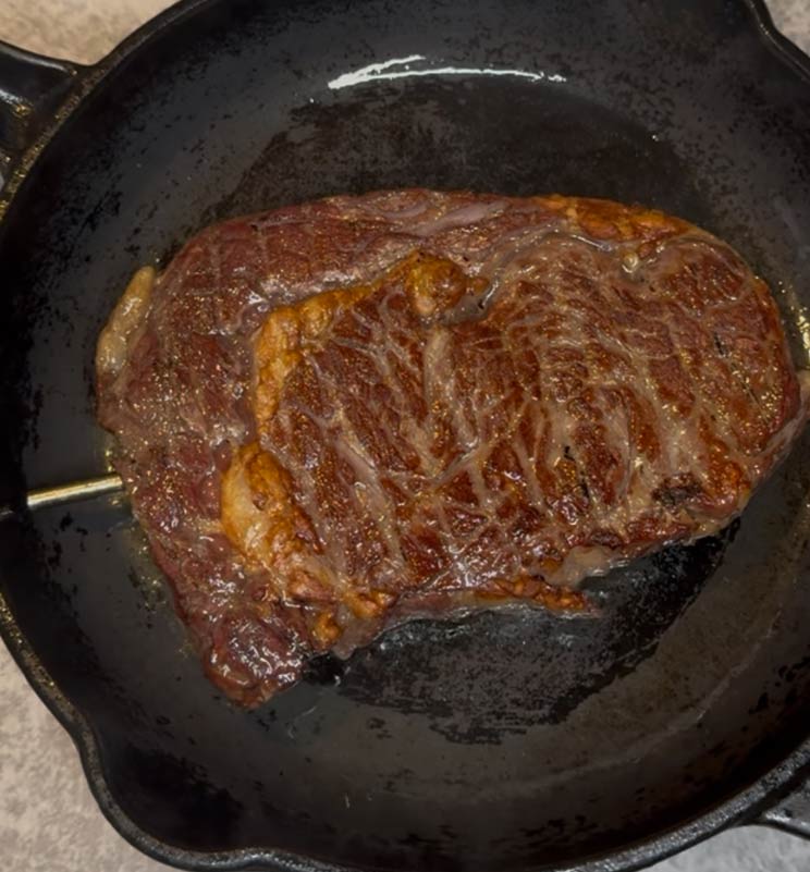 A thick ribeye steak developing a beautiful, golden-brown crust as it sears in a hot cast iron pan, preparing for perfect doneness with the RFX monitoring its internal temperature