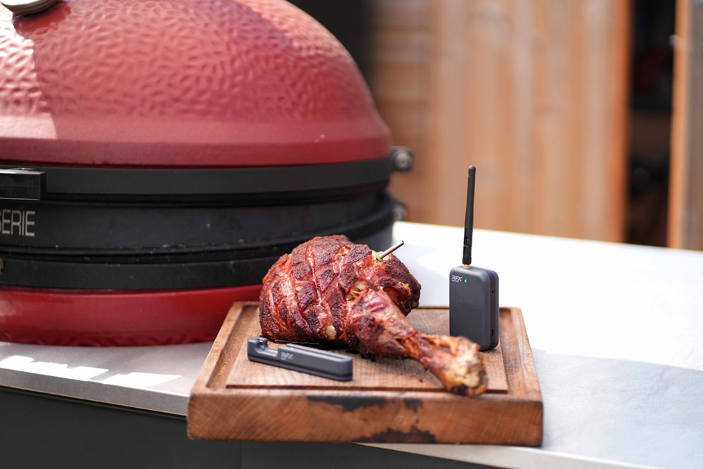 A leg of lamb on a wooden board in front of a red BBQ
