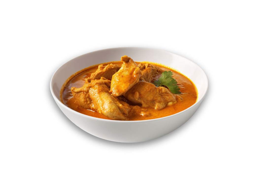 A vibrant orange-red chicken curry is served in a white bowl, against a pure white background. Several pieces of chicken breast are visible, submerged in the rich sauce.