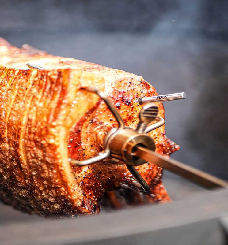 pork joint on a rotisserie of a kamado joe with thermapen rfx probe visible
