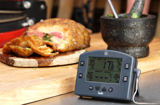A BBQ Smoke thermometer positioned in front of a cooked pork and herb dish