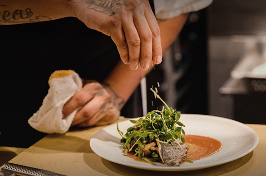 A chef garnishing a plate of food in a professional style kitchen