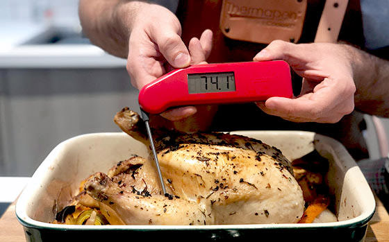 A red Thermapen digital food thermometer being used to read the internal temperature of a chicken