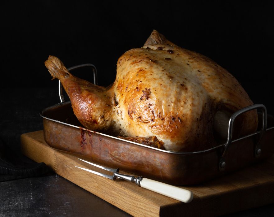 A perfectly roasted turkey in a copper roasting pan, sitting on a wooden cutting board.