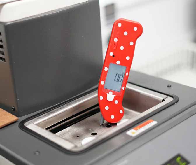 Finger and hand visible to hold the Thermapen ONE in red in place for an accuracy check in a calibration bath, screen is reading 100 degrees