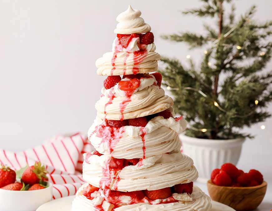 Christmas tree shaped cream coloured pavlova with red jam falling out between the layers