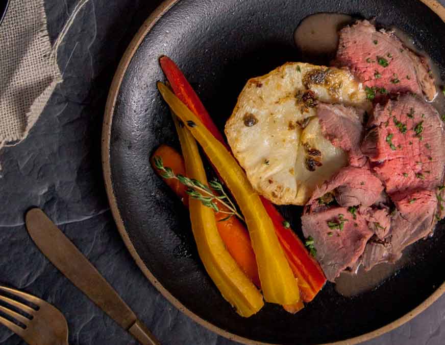 Roast beef, and vegetables on a black plate