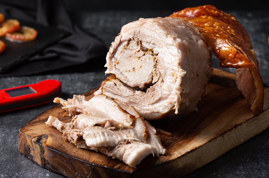 A porchetta which has been cooked to temperature with a Thermapen food thermometer, placed on a wooden chopping board